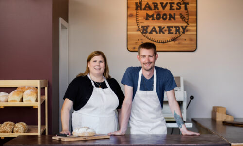 Husband and wife stand next to each other in their bakery, Harvest Moon Bakery on the North Shore in Kamloop, BC.